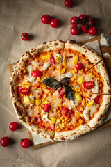 Pizza on the Board top view. Juicy pizza with chicken, pineapple and red tomatoes on a wooden Board and Kraft paper