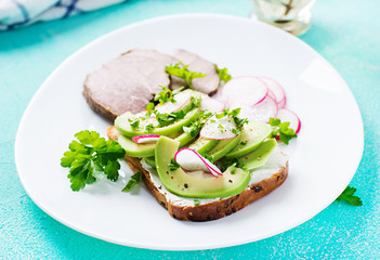 Tasty breakfast. Healthy avocado toast and radish on whole grain bread and baked sliced meat.