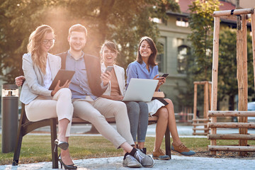 Happy business people sitting together during meeting outdoors  on a bench in the city.