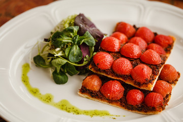 vegetarian pizza with cherry tomatoes, served with fresh herbs on a round white plate. on a wooden table top decorated with ceramic tiles