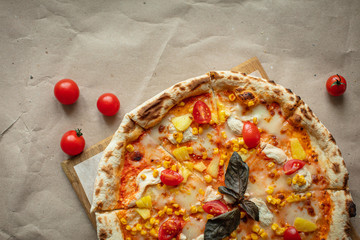 Pizza on the Board top view. Juicy pizza with chicken, pineapple and red tomatoes on a wooden Board and Kraft paper