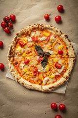 Pizza with chicken and pineapple, cheese, sauce and cherry tomatoes. The view from the top on the table and Kraft paper