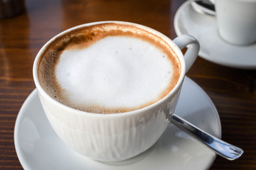 Simple coffee cup with milk foam on a white ceramic plate, on wooden background.