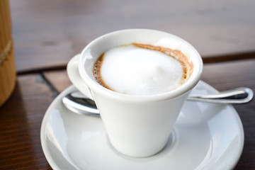 Simple coffee cup with milk foam on a white ceramic plate, on wooden background.