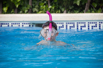 a boy with goggles, a pipe and a mask swims in the pool and green bushes for vacations, games