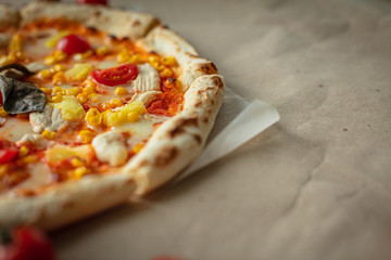 Closeup of pizza with chicken, pineapples, corn, tomatoes cherry. On Kraft paper.