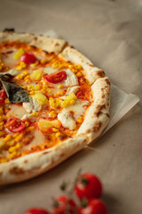Pizza with chicken and pineapple, cheese, sauce and cherry tomatoes. The view from the top on the table and Kraft paper