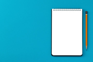Notepad copy space and pencil on a blue background top view.
