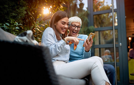 mother and daughter watching cell phone, smiling and laughing