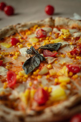 Closeup of pizza with chicken, pineapples, corn, tomatoes cherry. On Kraft paper.