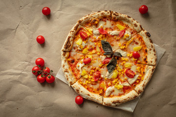 The pizza is big and round on the Kraft paper and wooden tray. Around the tomatoes and top view. The warm tones.