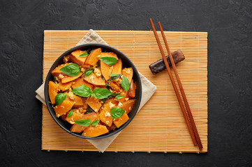 Pad Faktong or Thai Stir-fried Pumpkin in black bowl at dark slate background. Pad Phuk Tong is thailand cuisine dish with sliced Kabocha Squash, eggs or tofu and basil. Thai Food. Top view