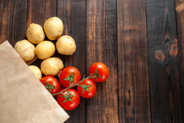 .Paper bag on a wooden brown background, vegetables from the store. Tomatoes, potatoes. Empty space for text.