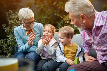 grandchildren sitting between grandparents on a sofa in the backyard learning how to clap hands