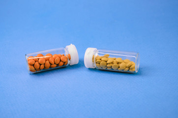 two glass packages with yellow and orange tablets lying with each other. on a blue background