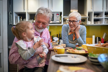 grandpa holding his granddaughter in a lap in a kitchen with grandma watching