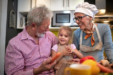 grandpa persuading his granddaughter to eat carrot. grandma watching and laughing