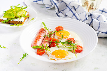 English breakfast - fried eggs, sausages, tomatoes and arugula. American food.
