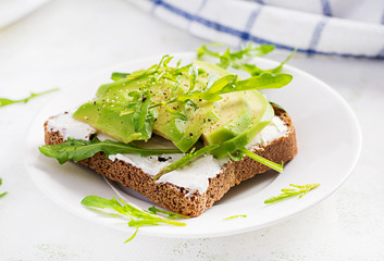 Sandwich of cream cheese bread and slices of avocado on a plate on a light background. Healthy vegetarian food.
