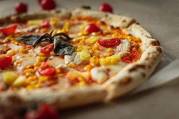 Closeup of pizza with chicken, pineapples, corn, tomatoes cherry. On Kraft paper.