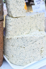 A sliced piece of cheese with dill and spices, for sale on counter top, during food festival.