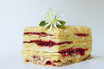 Piece of Napoleon cake with cherry jam decorating white flowers on the top. Food, dessert background.