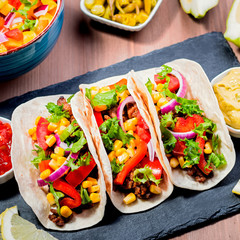 Table with tacos, mango salsa, nachos with sauce, guacamole, lemon beer. Appetizers and traditional mexican dishes for cinco de mayo or taco tuesday on wooden table top, copy space