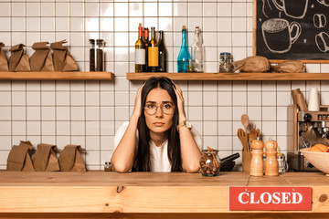 Upset cafe owner looking at camera near table with pepper and salt mills and card with  closed...