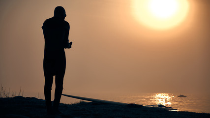 Closeup of a silhouette young surfer putting on wetsuit on beach. Lifestyle and sport concept.