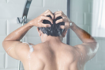 Closeup young man washing hair with with shampoo in the bathroom, vintage tone, selective focus