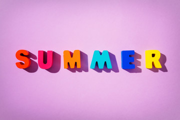 Flat lay composition with phrase SUMMER made of colorful wooden letters on top of purple background.