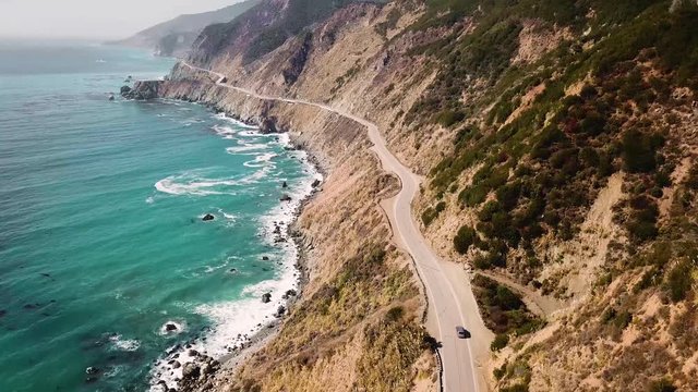 Aerial tracking shot of a car driving along a Pacific highway coast in California in USA.