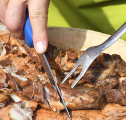 Man cutting grilled meat on cutting board, chefs hands with fork and knife