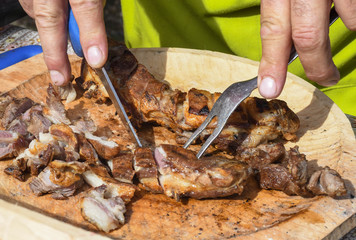 Man cutting grilled meat on cutting board, chefs hands with fork and knife