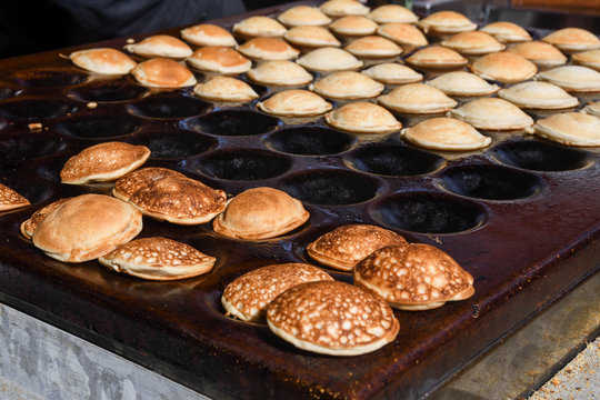 Typical Dutch poffertjes - tiny pancakes-being baked on a heavy cast iron pan