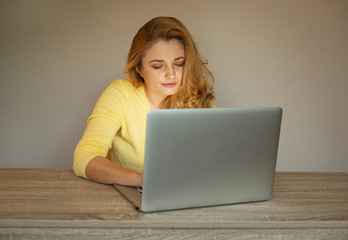 Young woman is working online. Girl with laptop. Smiling woman in  a yellow cardigan