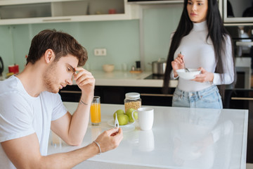 ill man holding thermometer while woman holding bowl with breakfast at home during self isolation, selective focus