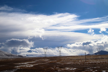 Plateau, high-voltage transmission tower, blue sky and white clouds, ice lake and distant Shishapangma Peak