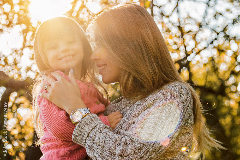 Wall mural portrait of young tender mother hugging her little cheerful daughter while standing outdoors. beauti