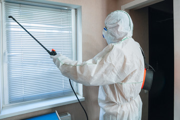 Coronavirus Pandemic. A disinfector in a protective suit and mask sprays disinfectants in house or...