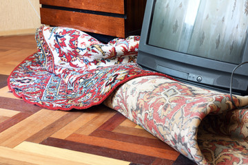 Fototapeta na wymiar The old TV is lying on a rolled-up carpet on the floor. The room has a mess, repairs, spring cleaning.The interior in the style of the 90s. Old design in the house.