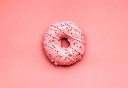 Creative still life food concept photo of a painted donut on pink background.