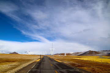 Sunny after the snow, the hut on the pasture, the snowy mountains in the distance, the blue sky and white clouds, the road leading to the distance, the high-voltage power transmission line, the very s