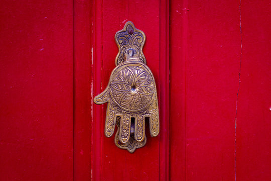 Hand of Fatima, a typical Moroccan design, as a door knocker on a red wooden front door - Powered by Adobe