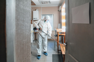 Coronavirus Pandemic. A disinfector in a protective suit and mask sprays disinfectants in house or...