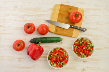 two white bowls with fresh salad of green cucumbers, red tomatoes and bell peppers on light wooden surface. Vegetables. Lowcalorie vitamin dietary food. Concept of healthy lifestyle