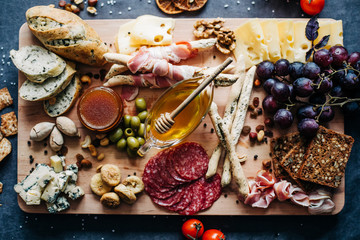 a set of beautiful and expensive products on a wooden Board cheese honey bread nuts and dried fruits and cherry tomatoes sliced sausages and olives