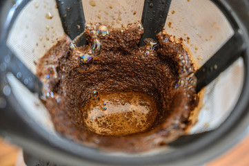 A high angle closeup shot of ground coffee in a drainer under the lights
