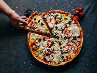 a man takes a slice from a pizza 40 cm top view with olives and bell peppers