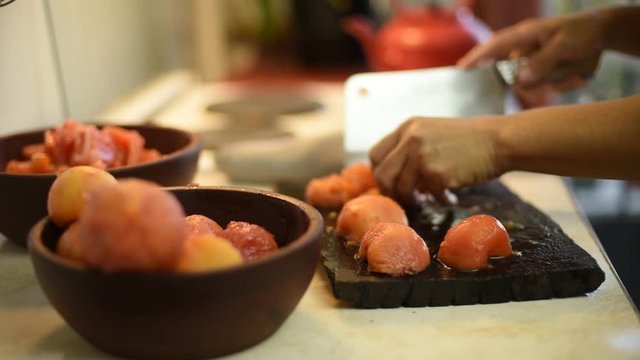manos cortando tomates sobre una tabla de madera
con cuenco lleno de tomates sobre mesada de una cocina
